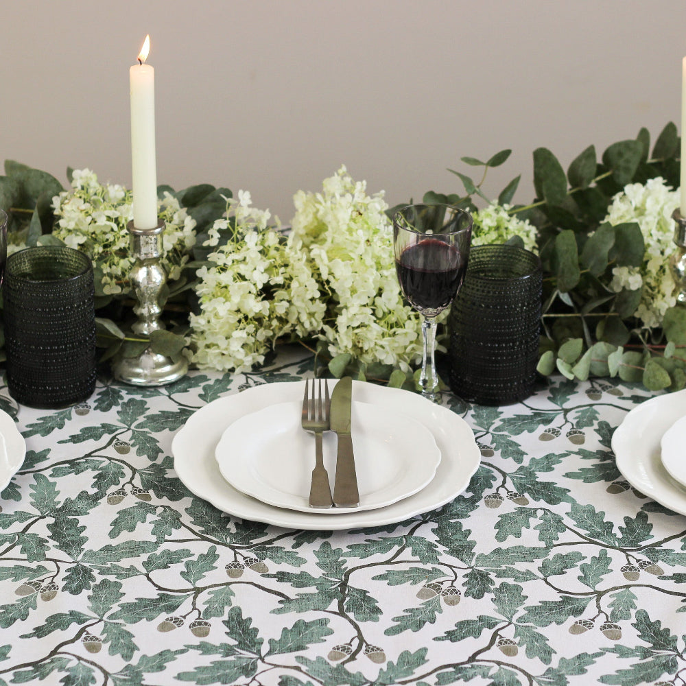 Elegant table setting with floral arrangement, candles, and cutlery on a patterned tablecloth.