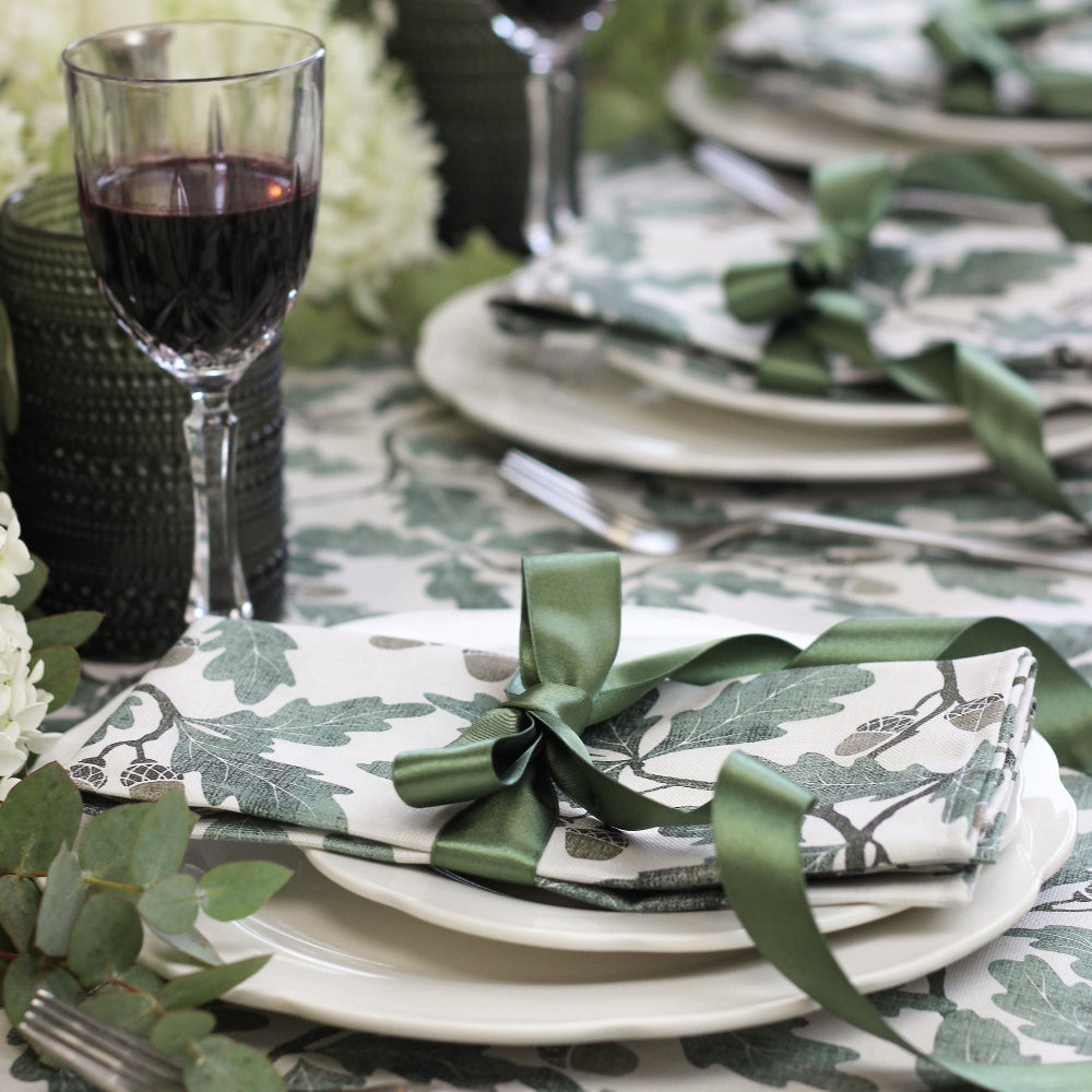 Elegant table setting with greenery-themed napkins and glasses on a patterned tablecloth.