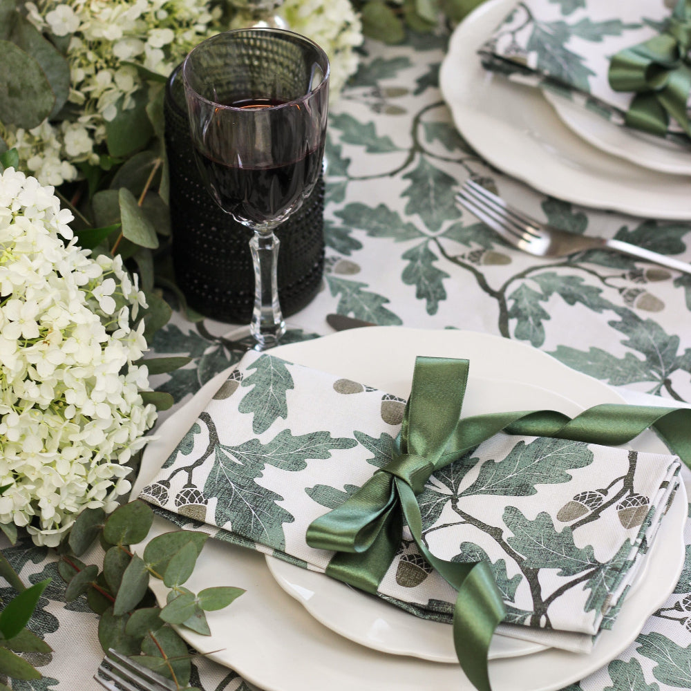 Elegant table setting with floral patterns and green ribbons on a leafy tablecloth.