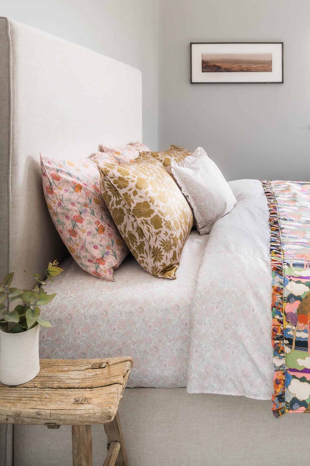 Bedroom with floral pillows and a colourful blanket on a bed, wooden bench, and framed picture on the wall.
