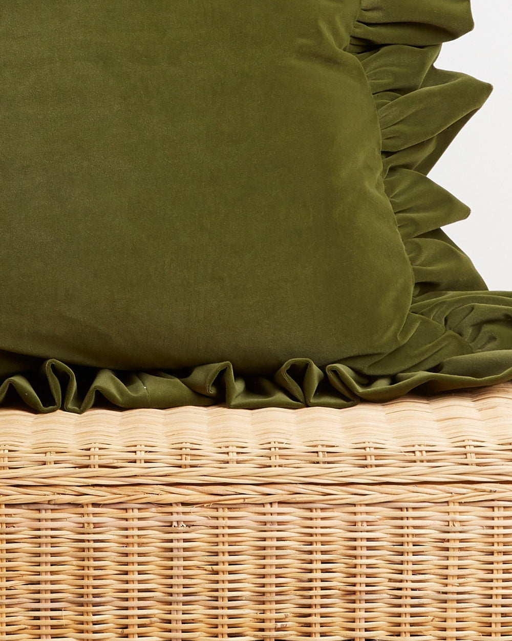 An forest green velvet throw pillow with ruffled edges resting on a light beige woven wicker basket.
