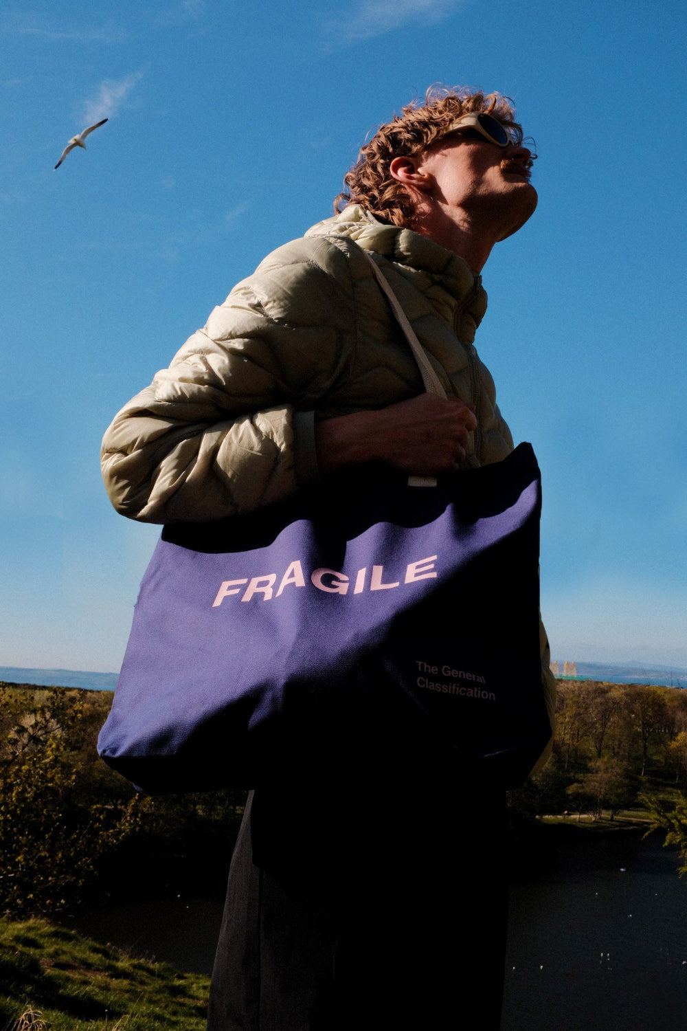 Person holding a purple 'FRAGILE' tote bag against a blue sky