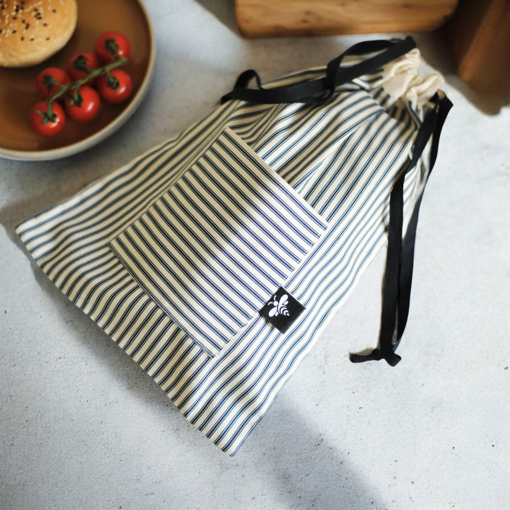 Striped drawstring bag on a light surface with a bowl of tomatoes and bread in the background