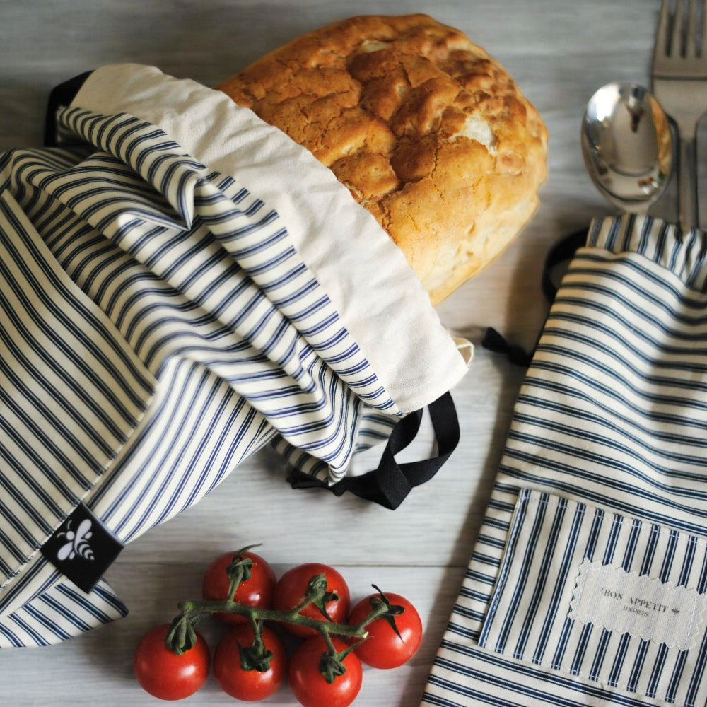 Striped bread bags with a loaf of bread and cherry tomatoes on a wooden surface
