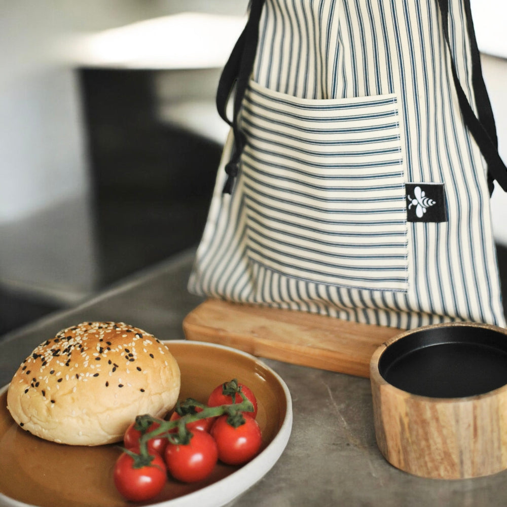 Bun with tomatoes on a plate next to a wooden container and striped apron.