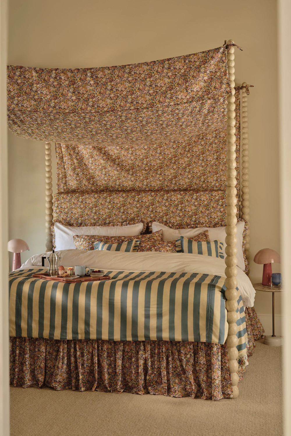 Four-poster bed with floral canopy and striped bedding in a bedroom setting.