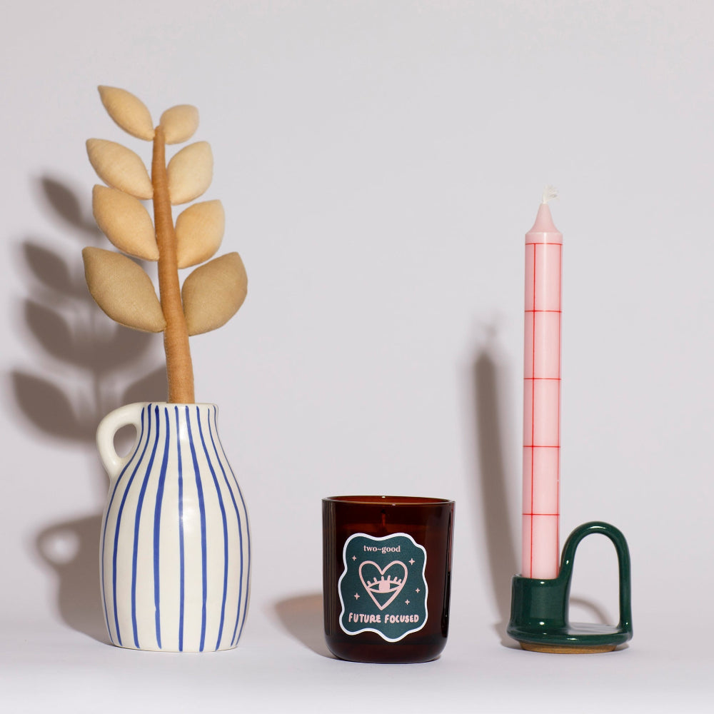 Decorative items including a vase with leaves, a candle, and a small container on a light background