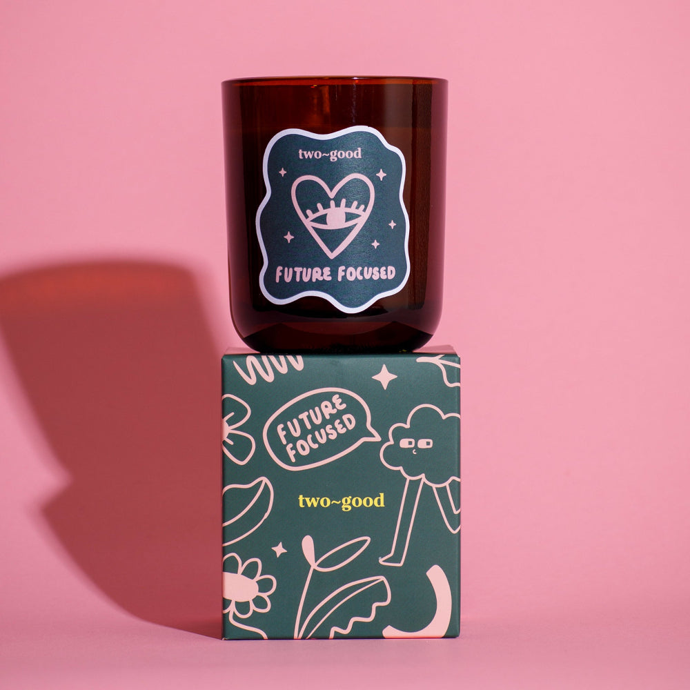 Candle with 'two-good' branding on a pink background