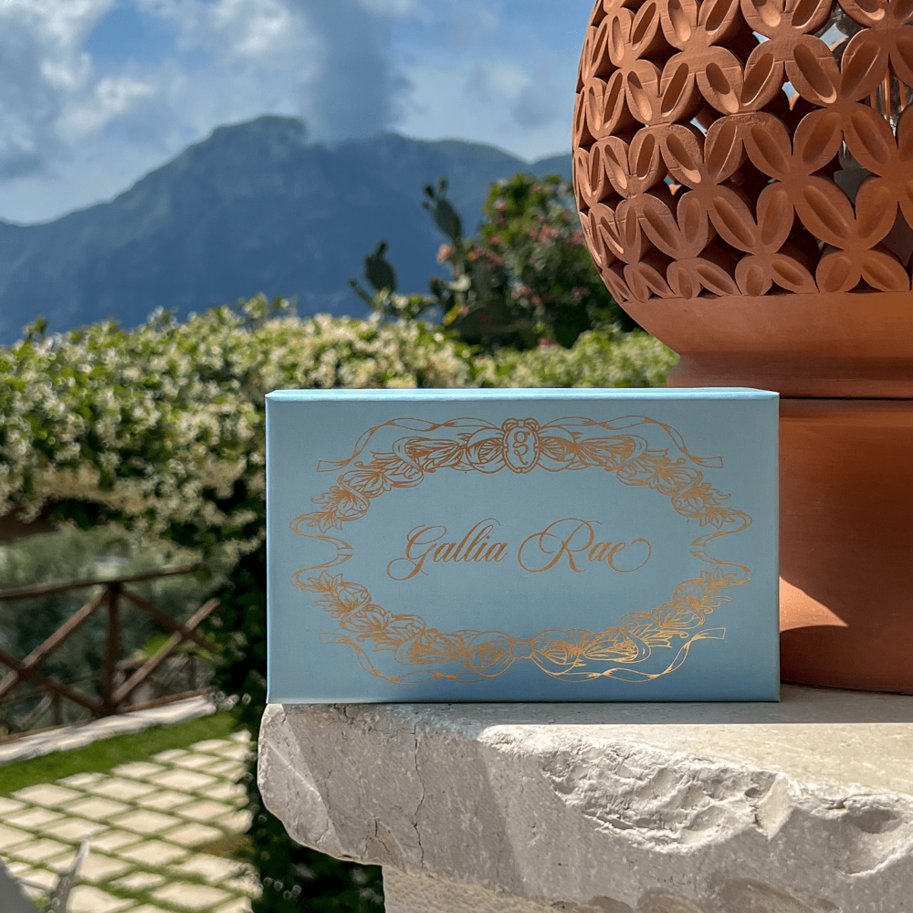 Blue box with gold text 'Gallia Rae' on a stone surface with a scenic background