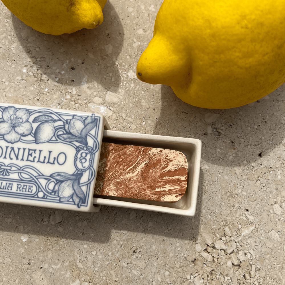 Small ceramic matchbox with home fragrance next to lemons on a concrete surface