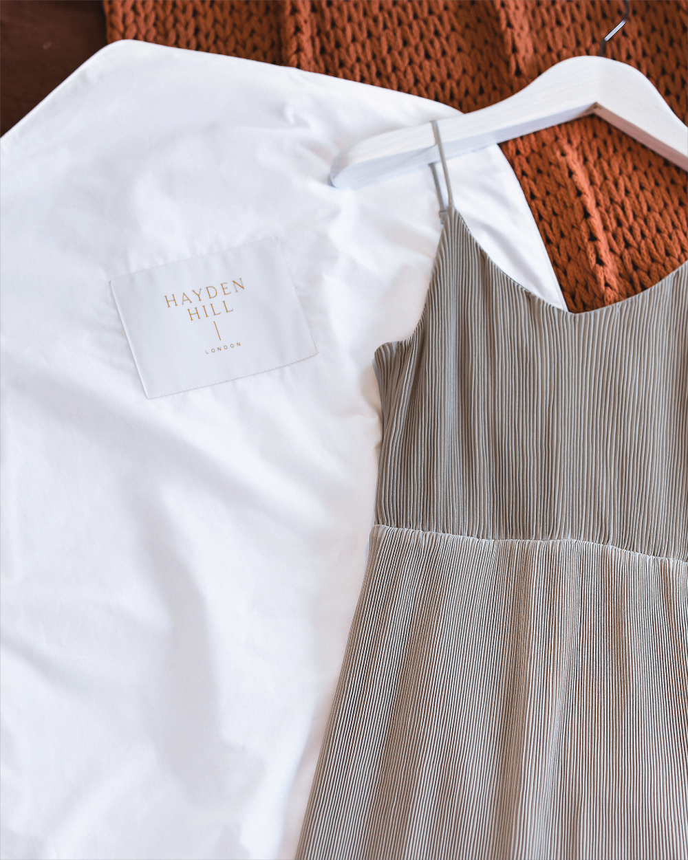 White protective hanging cover with 'Hayden Hill' logo on a hanger against a textured brown background