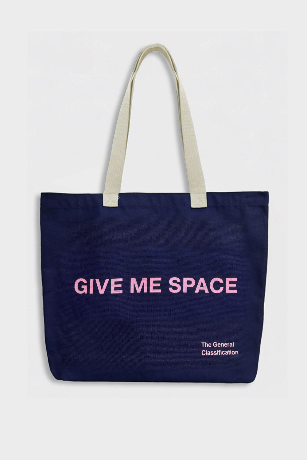 A navy blue canvas tote bag with cream-colored shoulder straps, featuring the text 'GIVE ME SPACE' in pink on the front, with 'The General Classification' printed in small white text below it. The bag is photographed against a clean, light gray background.