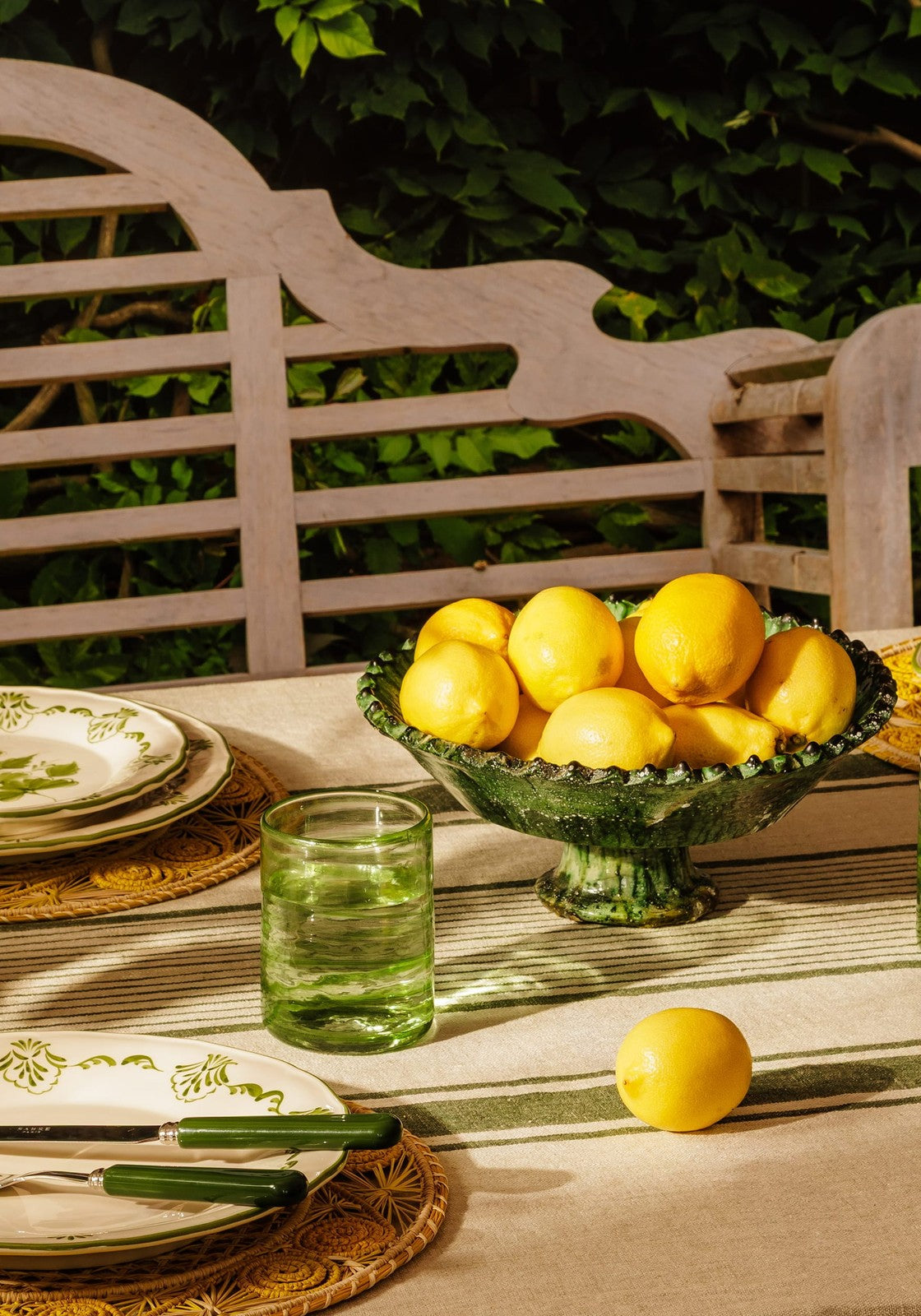 Outdoor table setting with lemons in a green glass bowl, plates, and glasses.