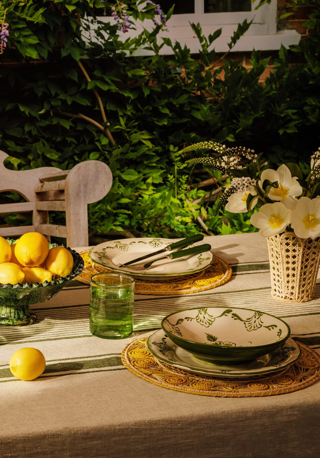 Outdoor dining setup with tableware, lemons, and flowers in a garden.