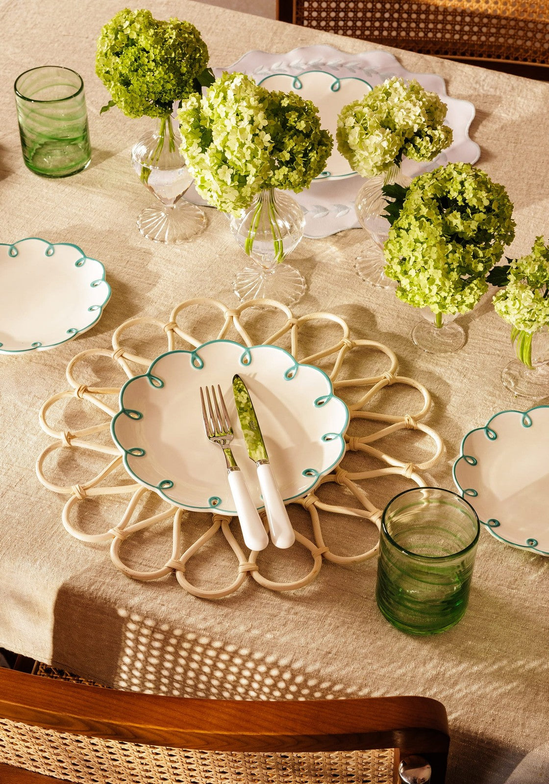 Table setting with green floral arrangements, plates, and glasses on a beige tablecloth.