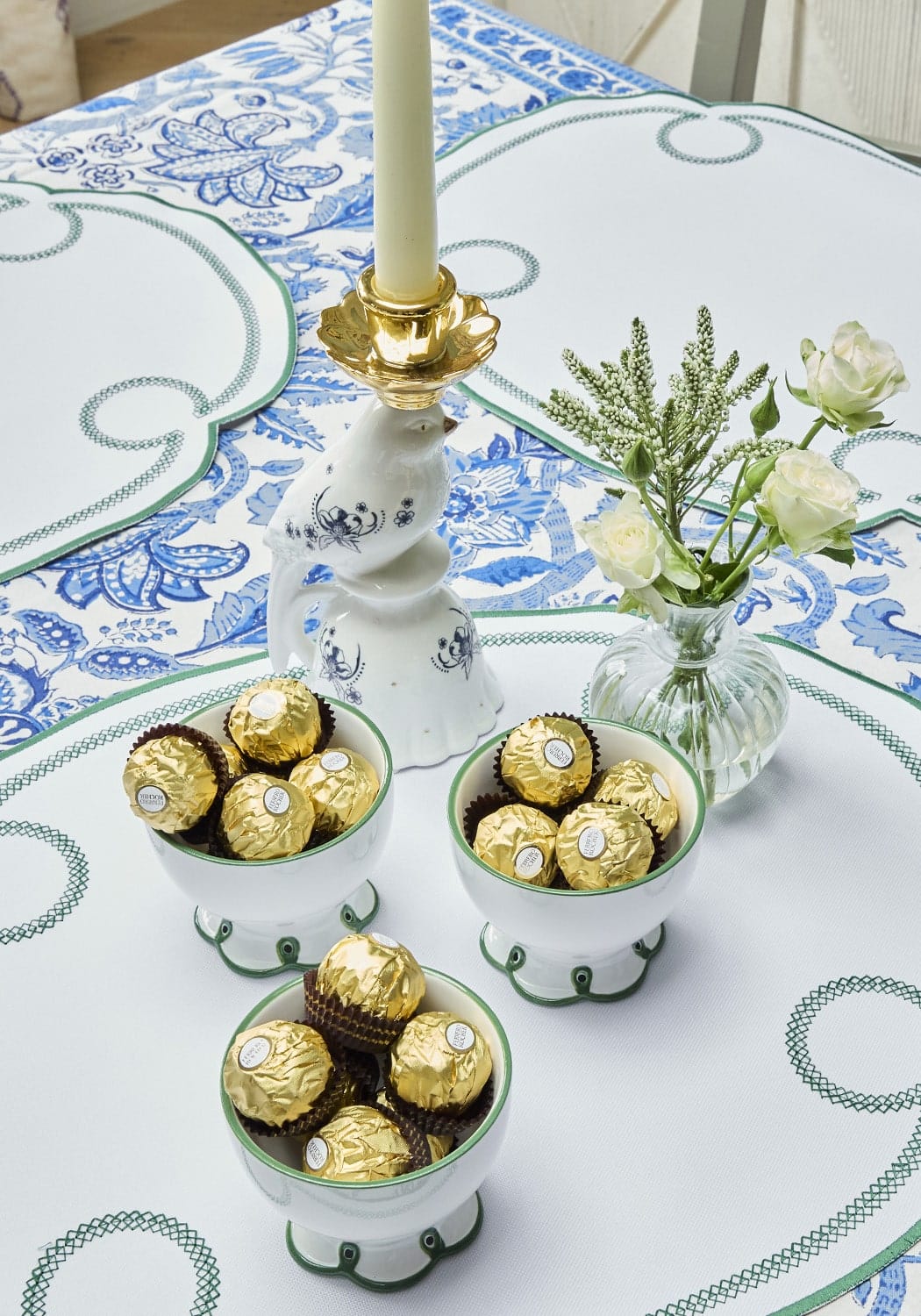 Decorative table setting with chocolates, a candle, and flowers on a patterned tablecloth.