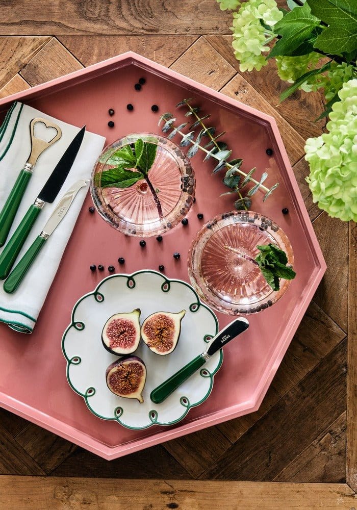 Pink tray with plates of figs, glasses, and cutlery on a wooden surface.