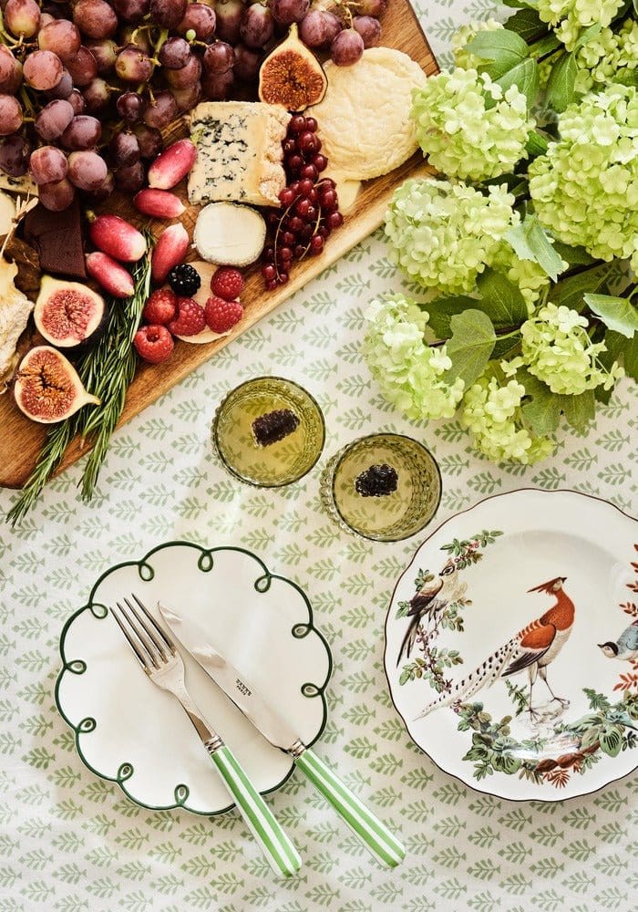 Table setting with a charcuterie board, plates, and flowers on a patterned tablecloth.