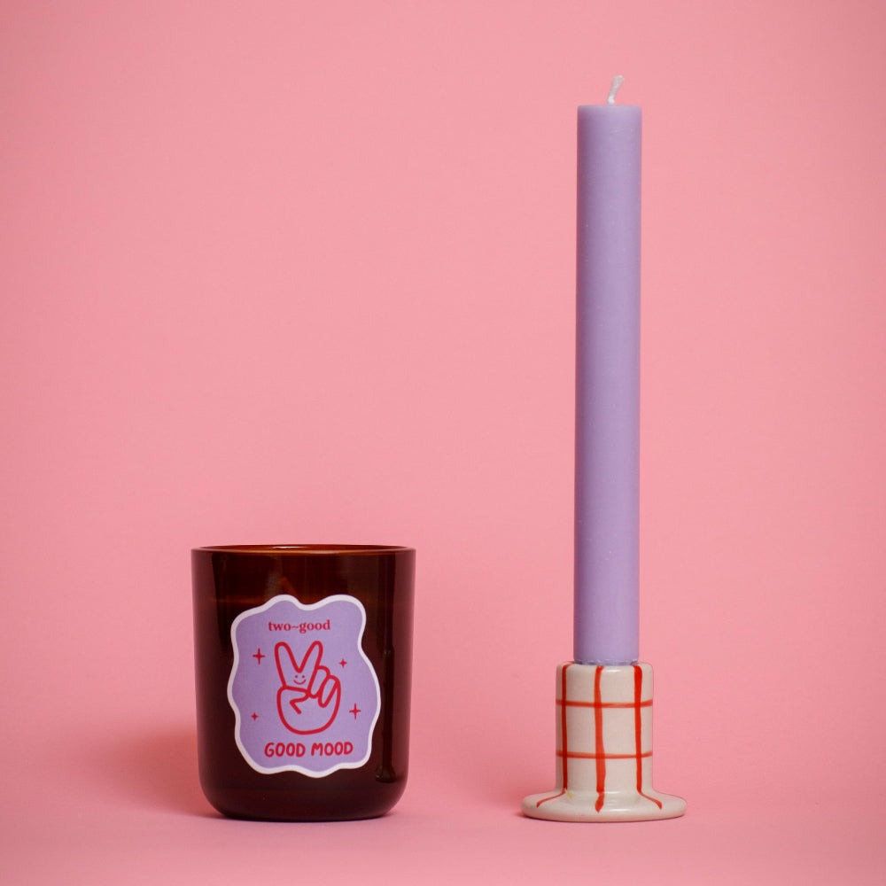 Candle Jar with two good branding called 'Good Mood' and a tall purple candle on a pink background