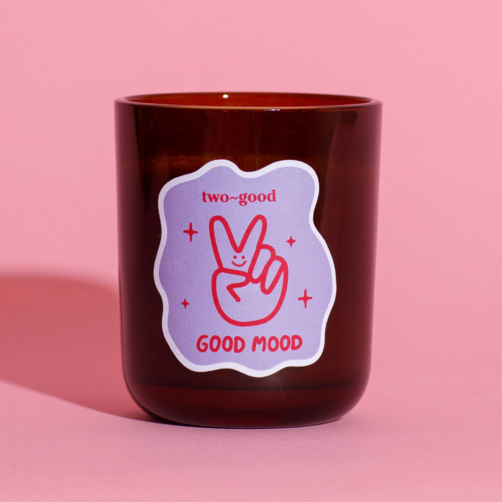 Brown candle with a 'two-good GOOD MOOD' label on a pink background