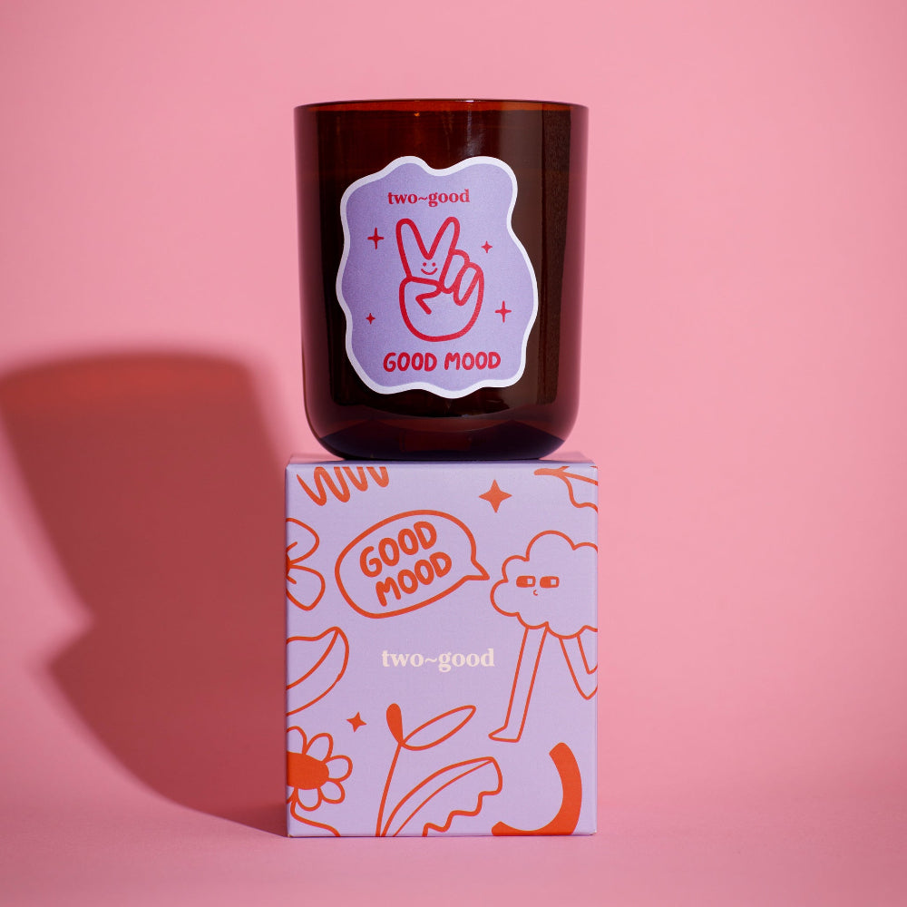 Candle with 'Good Mood' label on a matching box against a pink background