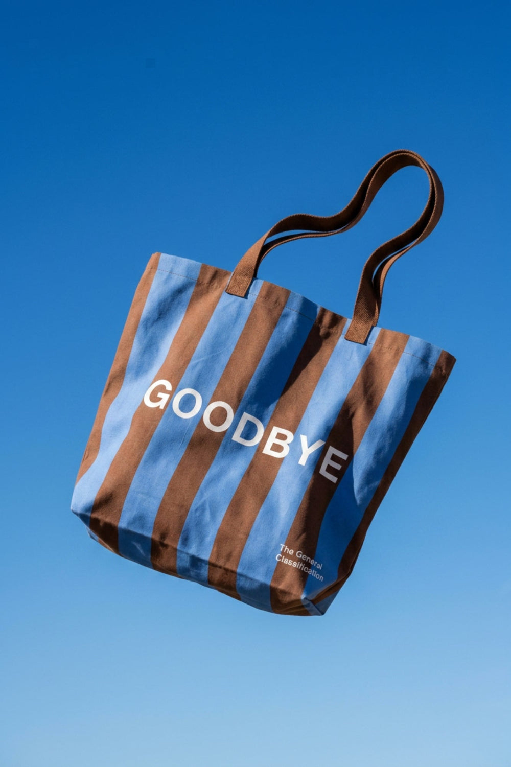 Striped tote bag with 'GOODBYE' text against a clear blue sky