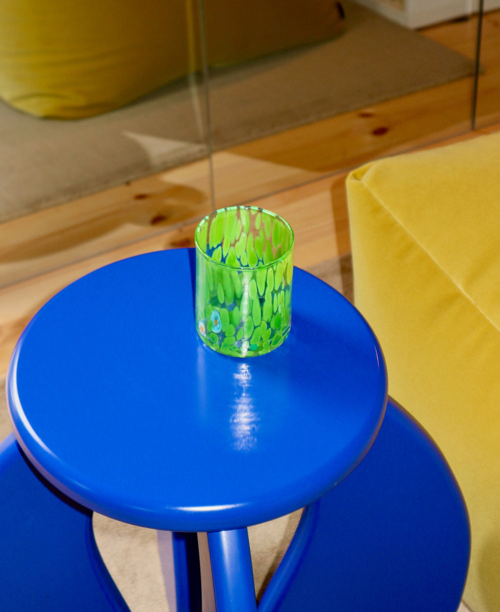 Blue stool with a green glass murano tumbler on a wooden floor