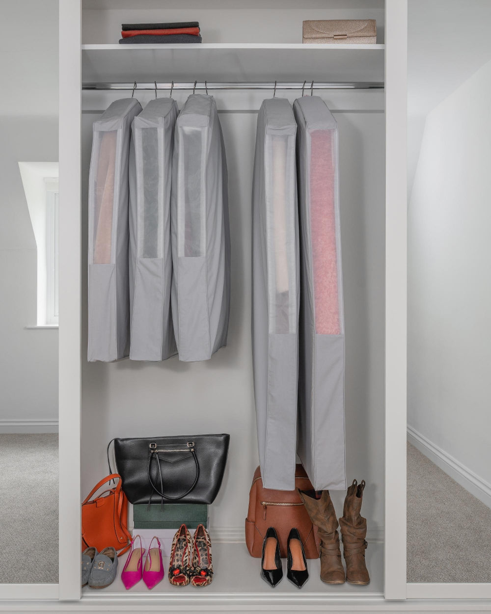 Closet with hanging clothes, shoes, and bags on a white shelf.