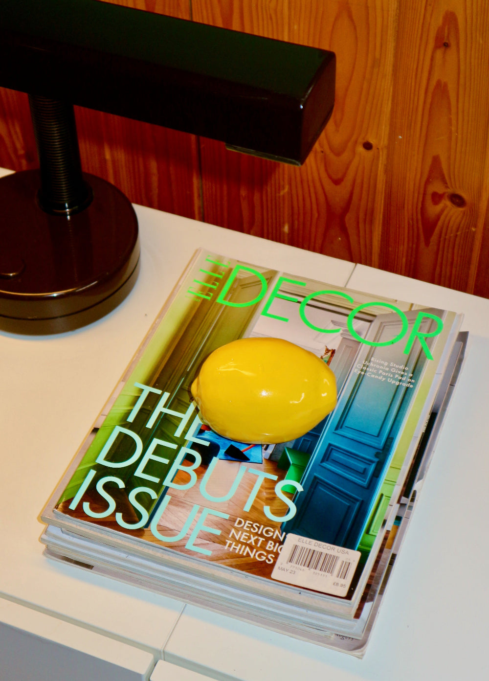 Decor magazine with a ceramic yellow lemon on top, placed on a surface with a lamp in the background.
