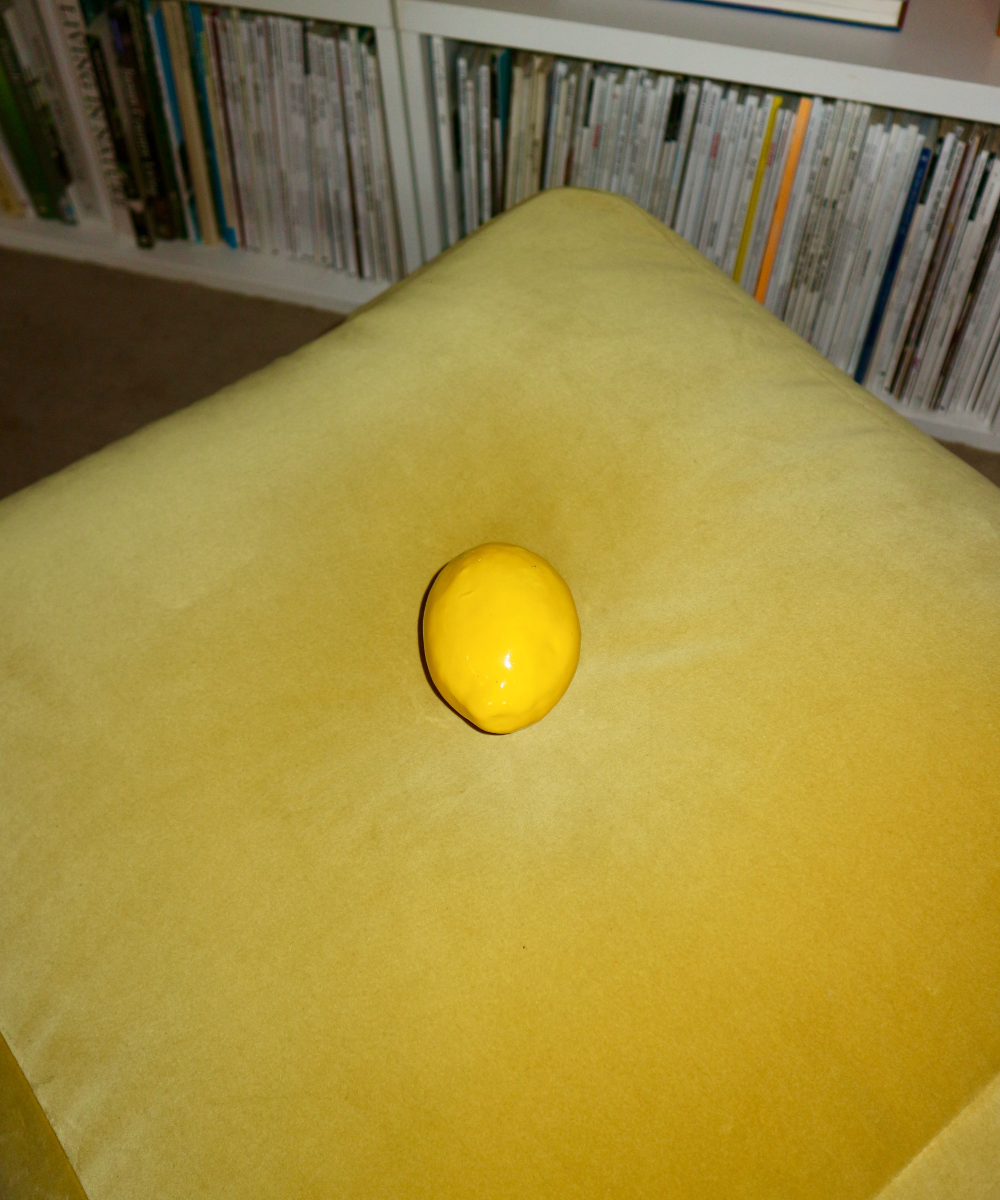 Yellow ceramic lemon on a yellow cushion with a bookshelf in the background
