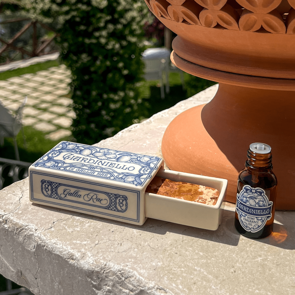Gardiniello Gialla Rea box with marble stone and a fragrance bottle on a stone surface outdoors.