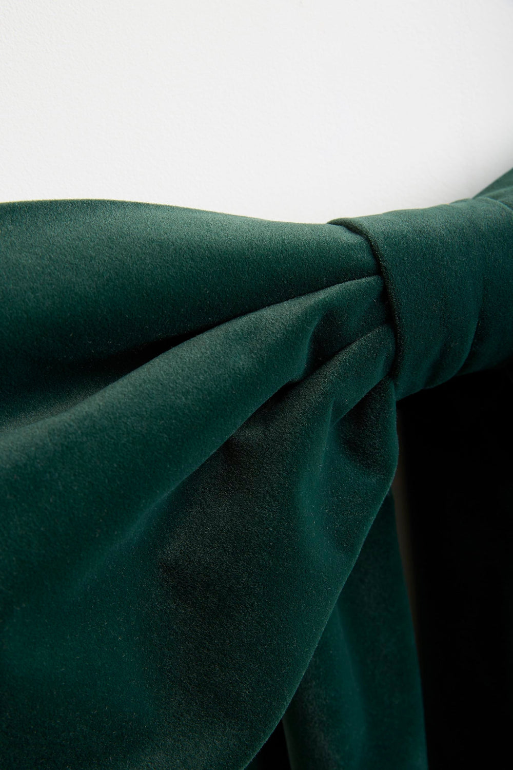 A close-up of dark forest green velvet fabric draped in soft folds against a light gray background.