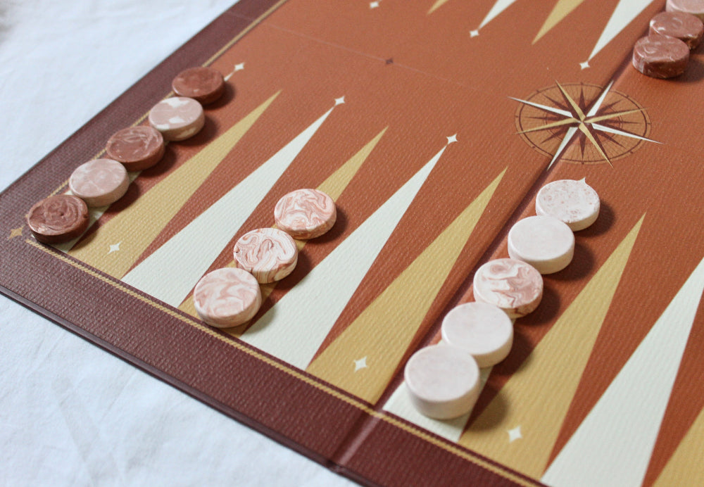 Close-up of handmade terracotta and white marbled Jesmonite backgammon counters arranged on the illustrated board.