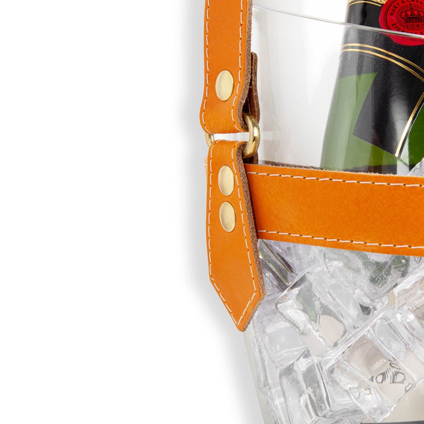 Clear champagne bucket with orange strap holding a bottle of wine and ice cubes on a white background