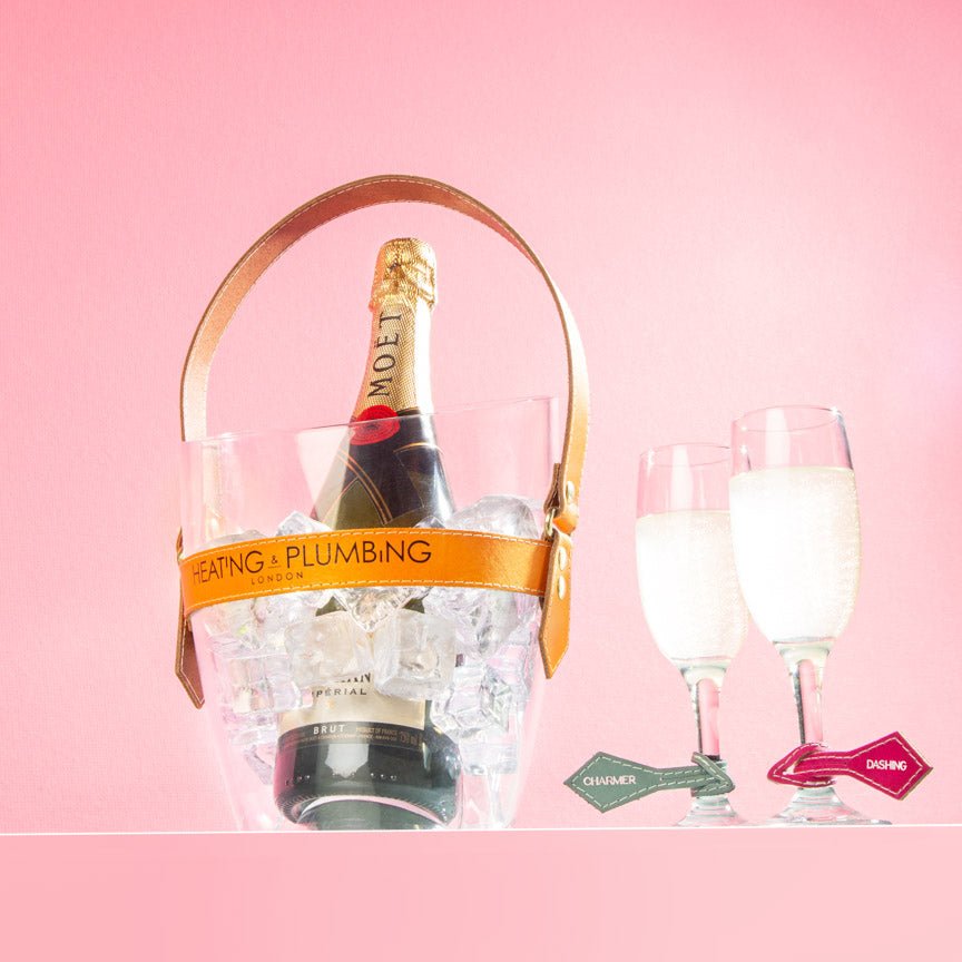 Champagne bottle in a ice bucket with glasses on a pink background