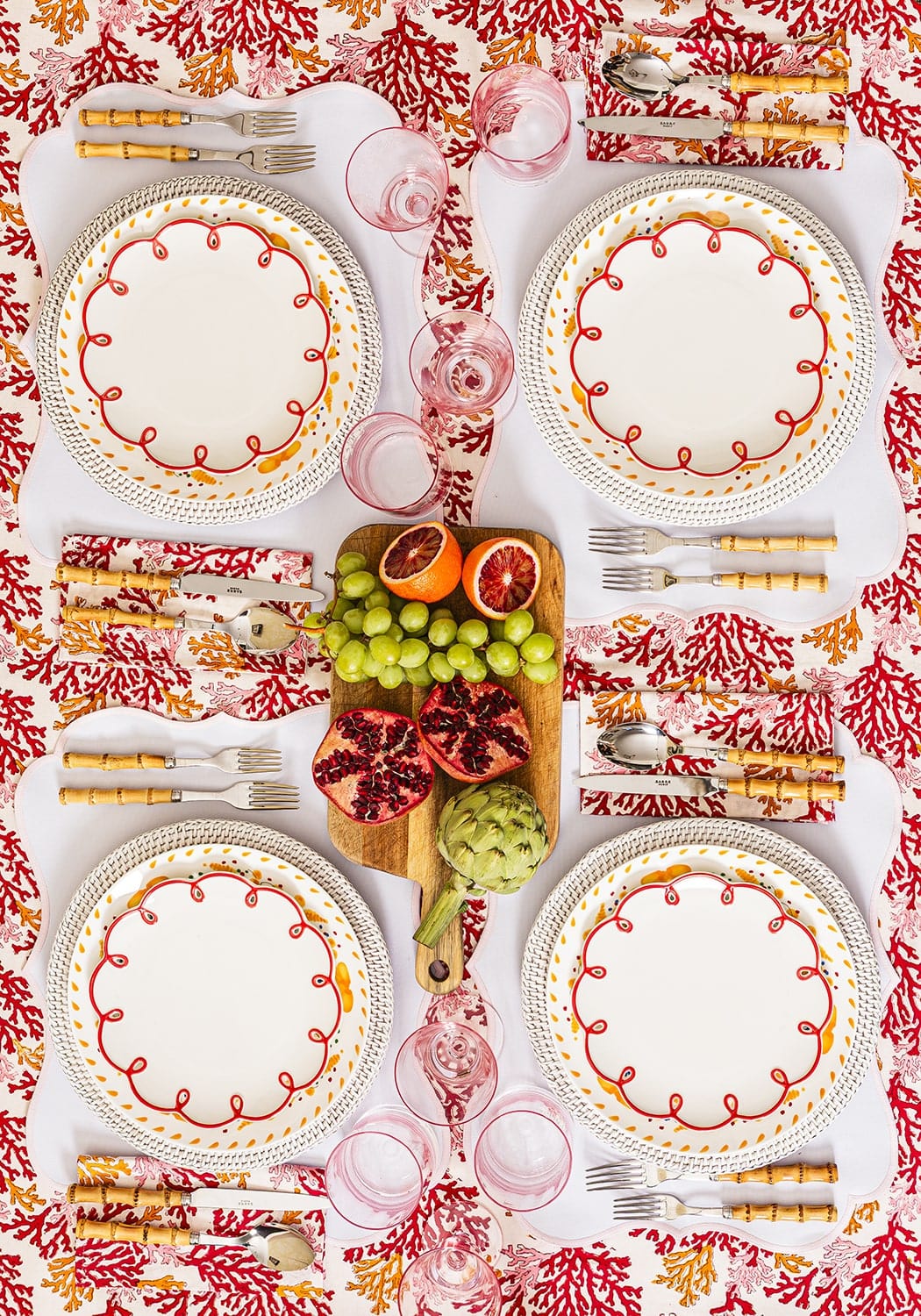 Dining table setting with plates, cutlery, and fruit on a red and white patterned tablecloth.