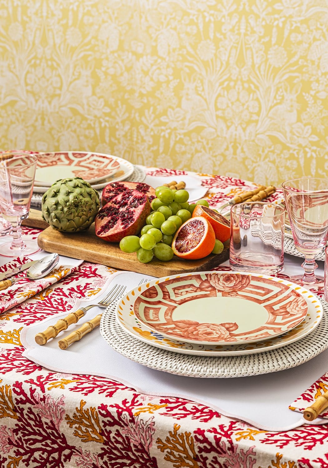 Dining table setting with fruit and plates on a patterned tablecloth.