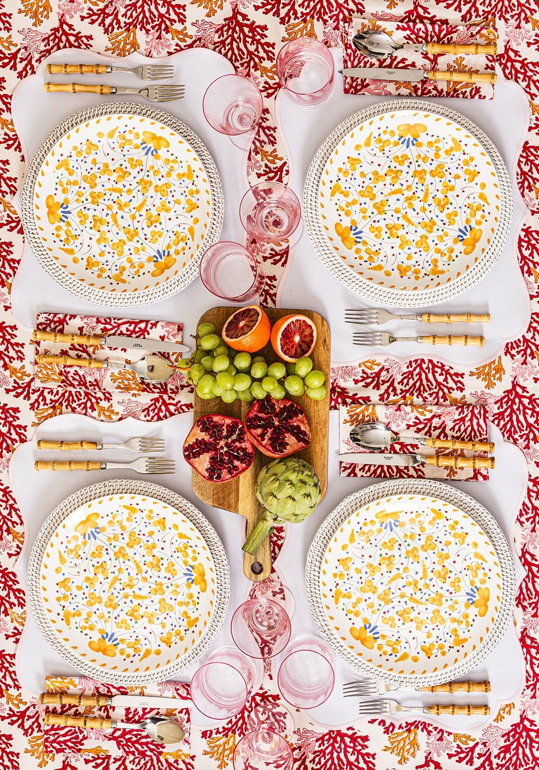 Dinner table setting with floral plates, fruits, and cutlery on a red and white patterned tablecloth.