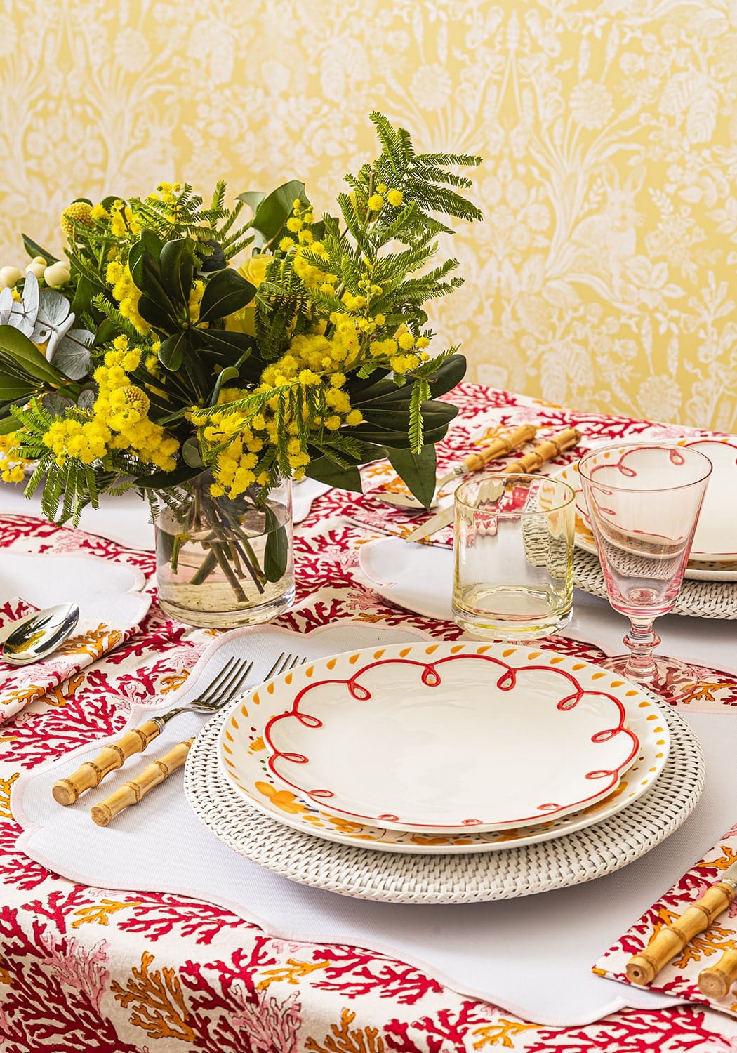 Decorative table setting with floral arrangement, plates, and cutlery on a patterned tablecloth.