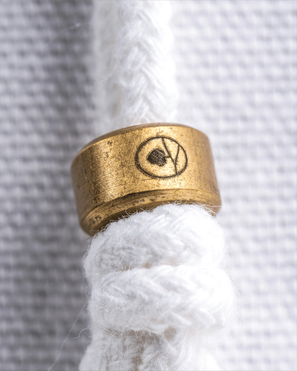 Brass ring with a symbol on a white rope against a textured white background