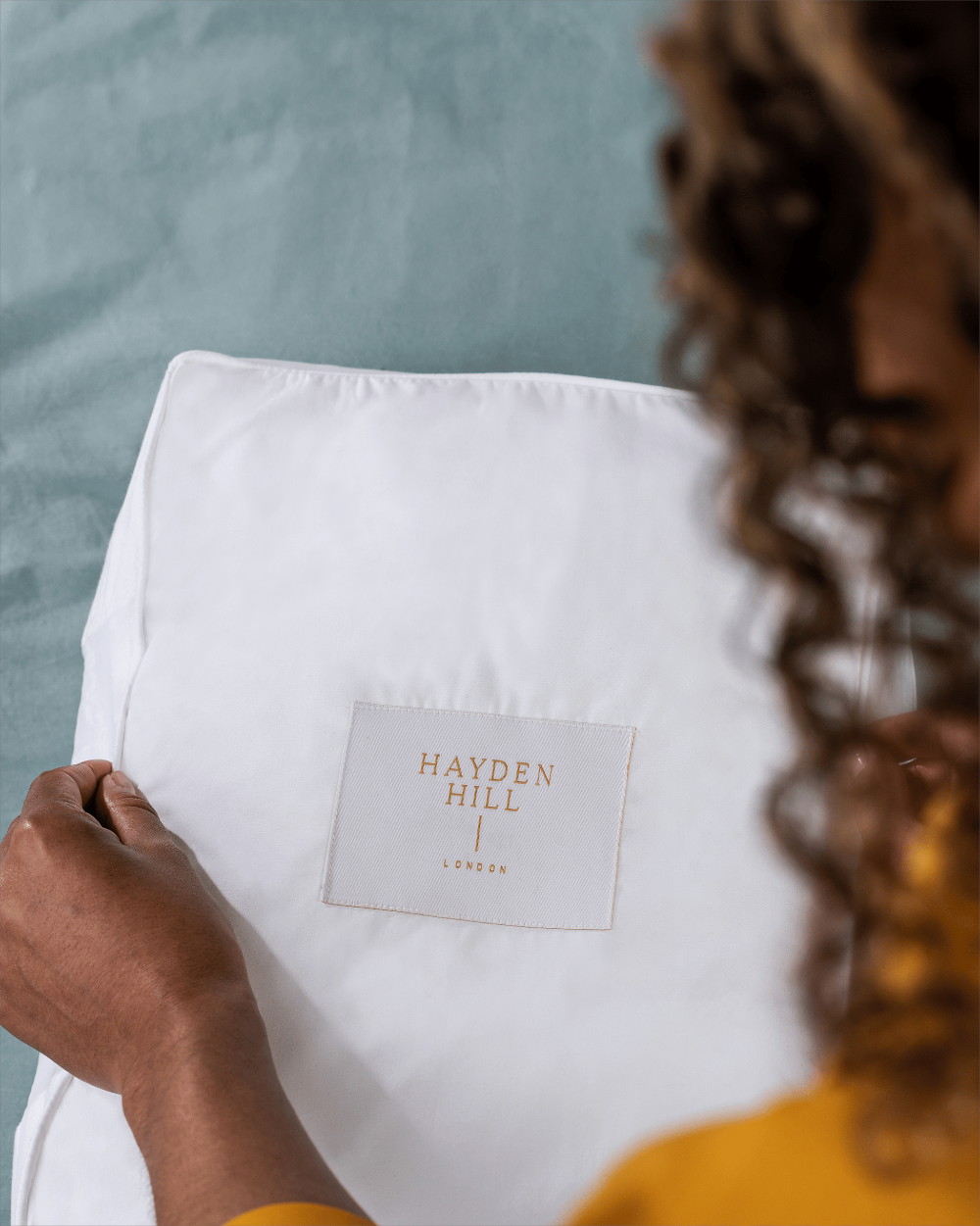 Person holding a white cotton storage bag with 'Hayden Hill' branding against a blurred background