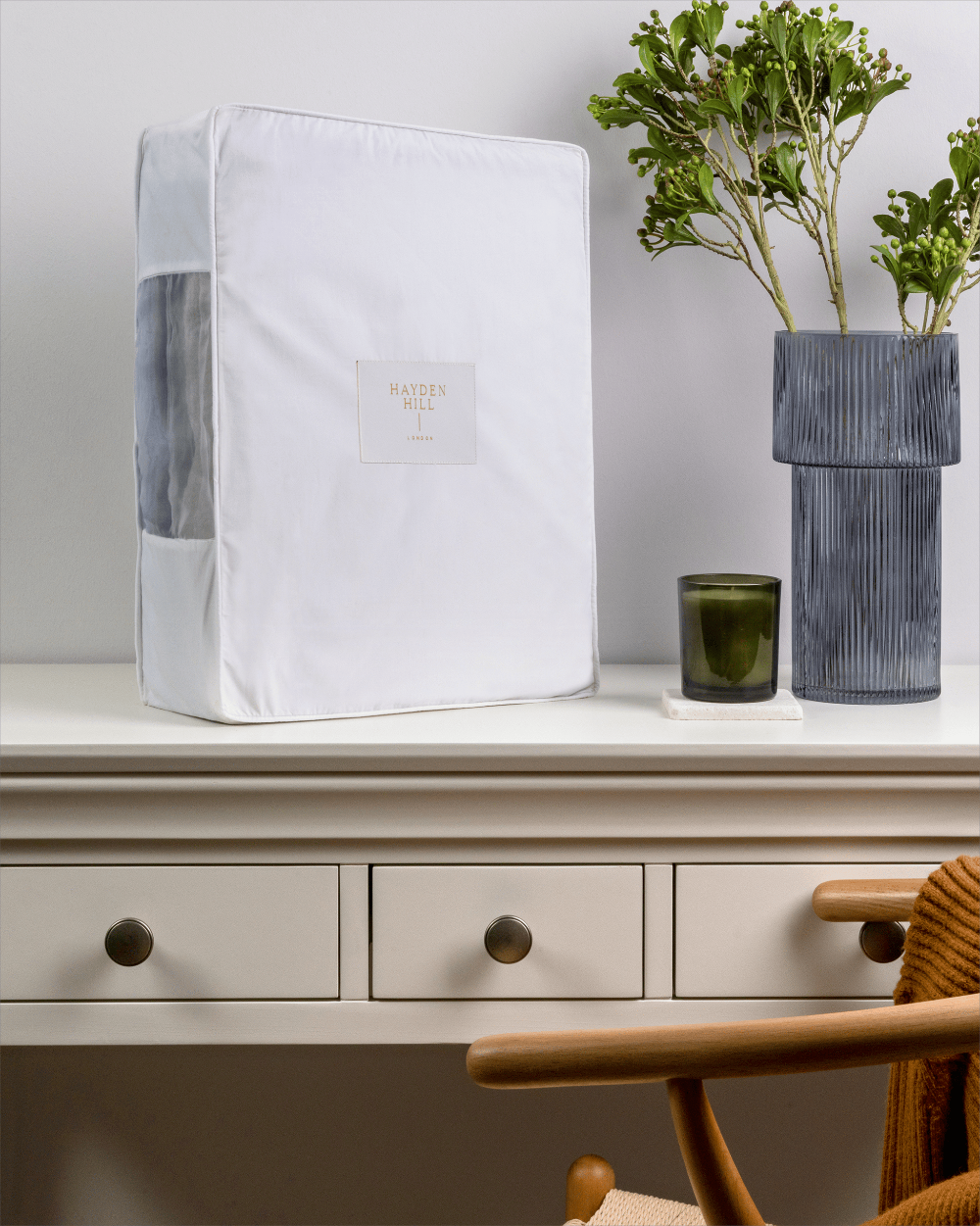 White storage clothes box with a brand logo on a white surface with a plant and candle in the background.