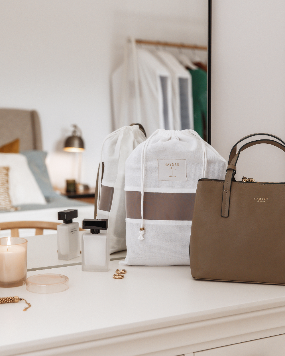 Brown handbag and white drawstring bag on a dresser with candles and jewelry.