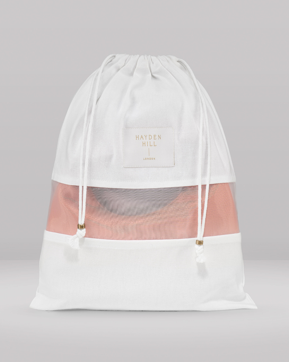 A white drawstring storage bag with a semi-transparent mesh front panel showing a pink garment inside. A square white label on the front reads 'HAYDEN HILL'
