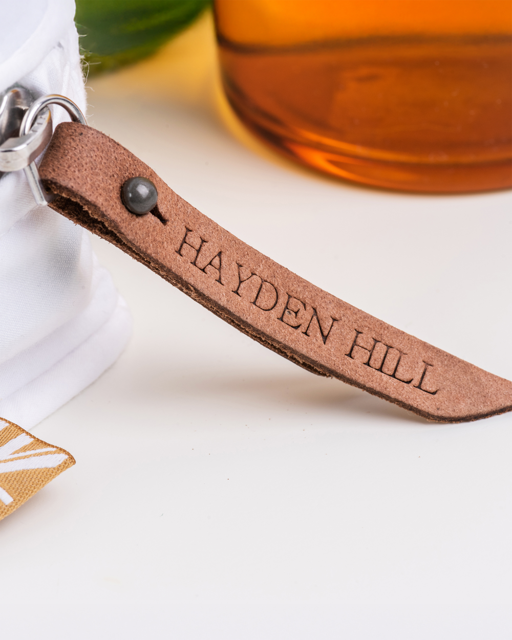 Leather keychain with 'Hayden Hill' engraving next to a bottle.