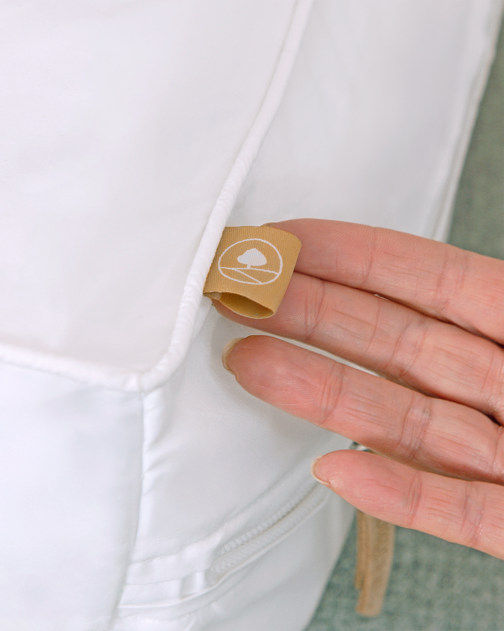 Hand holding a small brown label with a logo on a white shirt.