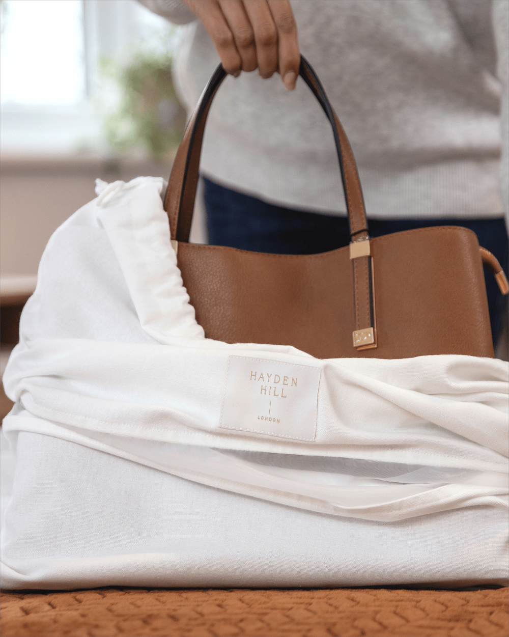 Brown handbag with 'Hayden Hill' label on a white storage dustbag