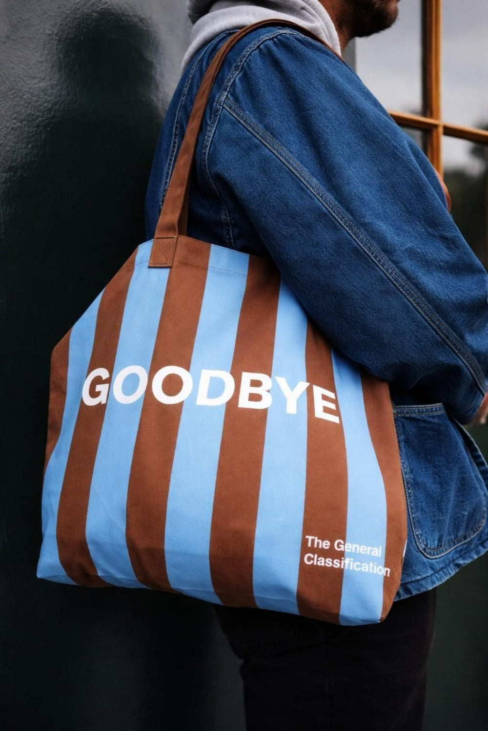 Person holding a striped bag with 'GOODBYE' text against a dark background