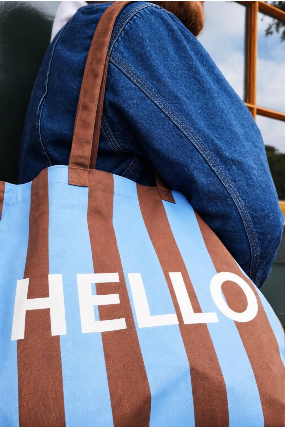 Striped tote bag with 'HELLO' text held by a person wearing a blue jacket.