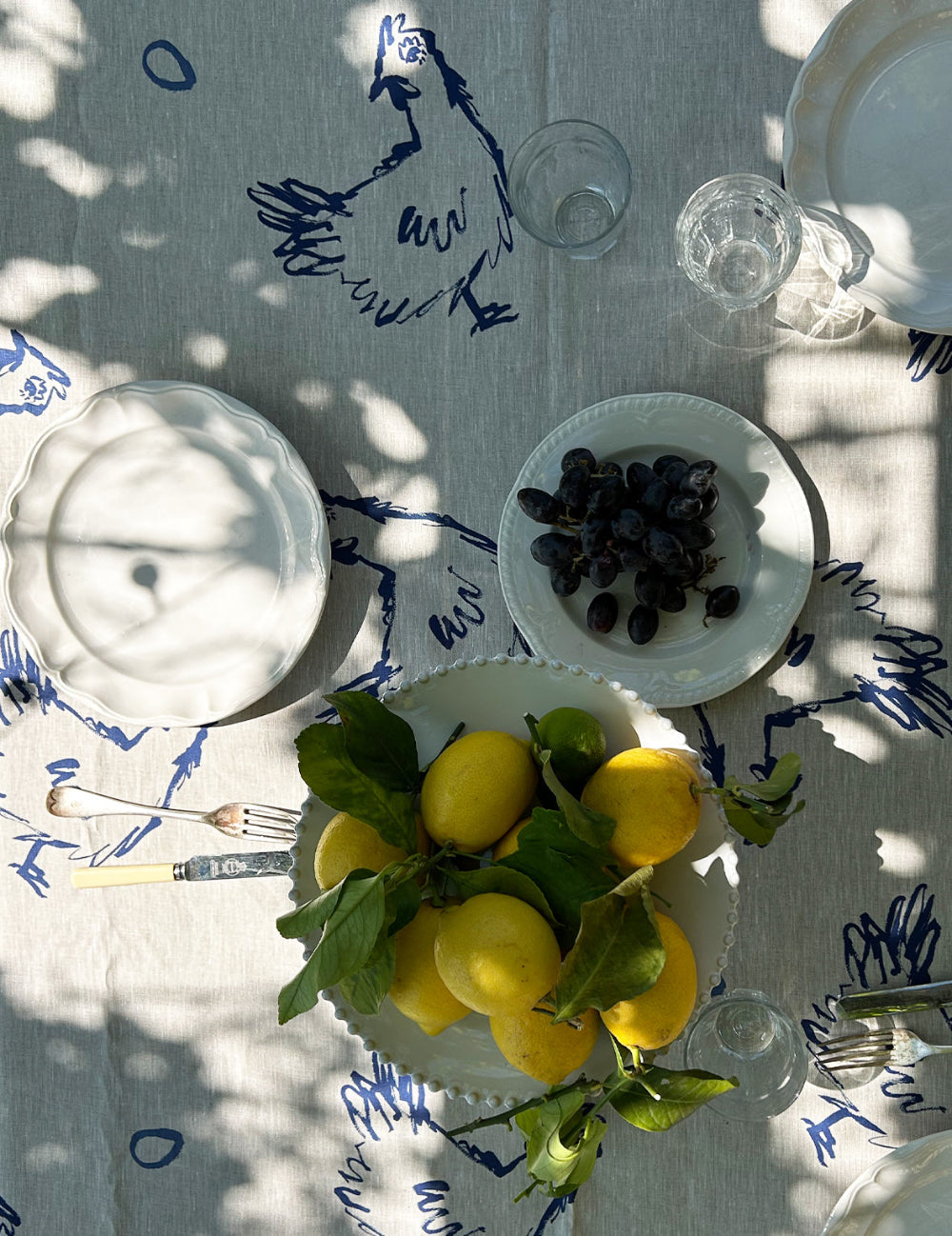 Table setting with lemons, grapes, and cutlery on a patterned tablecloth.